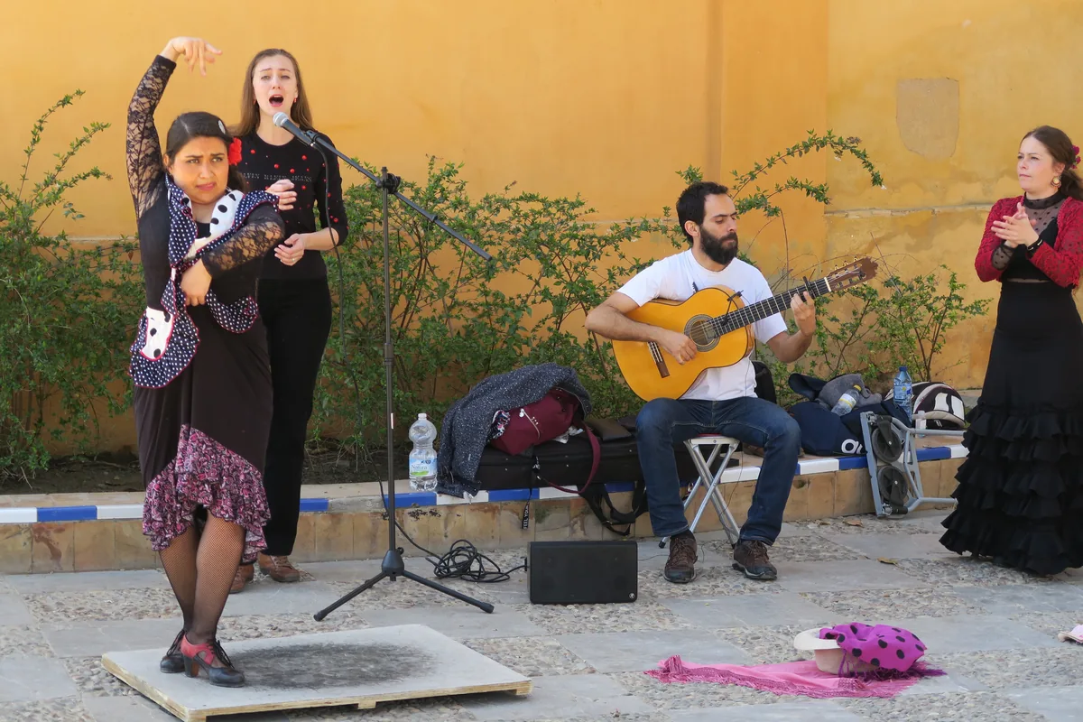 A flamenco dancer, a singer, a guitarist and a second dancer clapping, performing on a paved square in Seville in front of a yellow wall